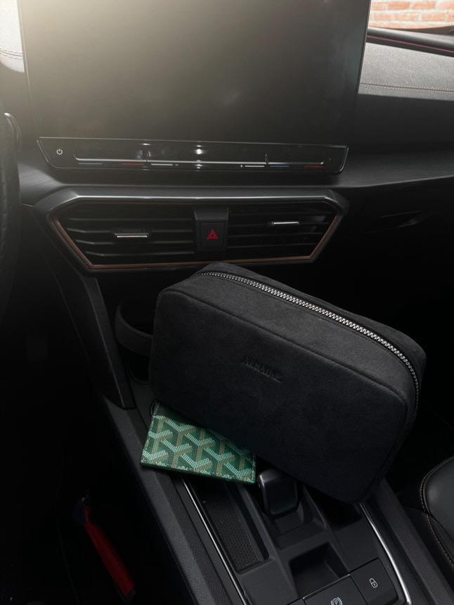 Luxe Alcantara toilettas van Alsaine in het middenconsole van een premium auto, naast een designer portemonnee